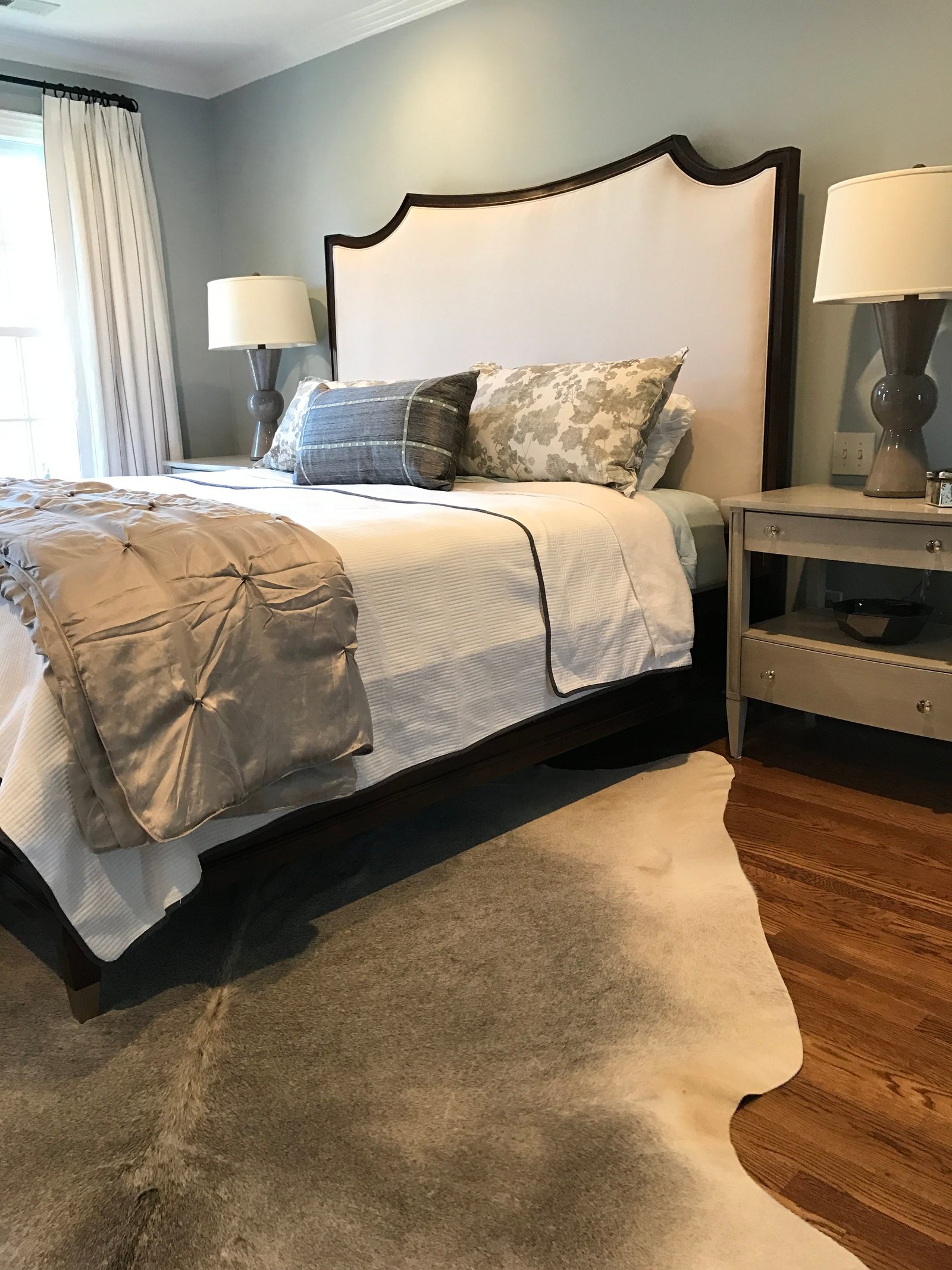 Bedroom with a curved upholstered headboard, a cowhide rug and a pair of gray lamps