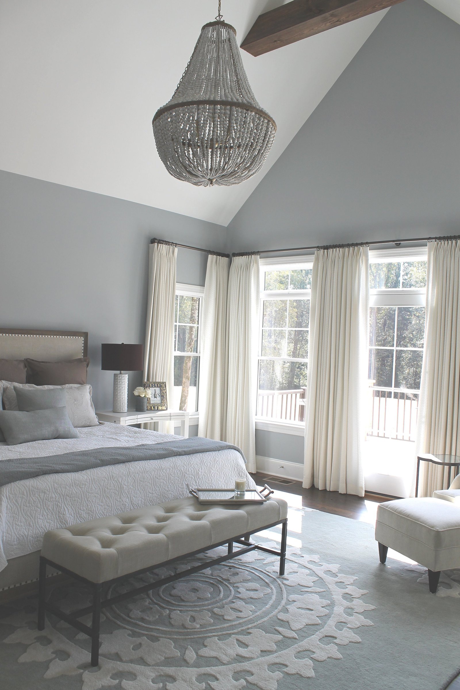 Serene gray bedroom with a vaulted ceiling, a beaded chandelier and a tufted bench at the foot of the bed