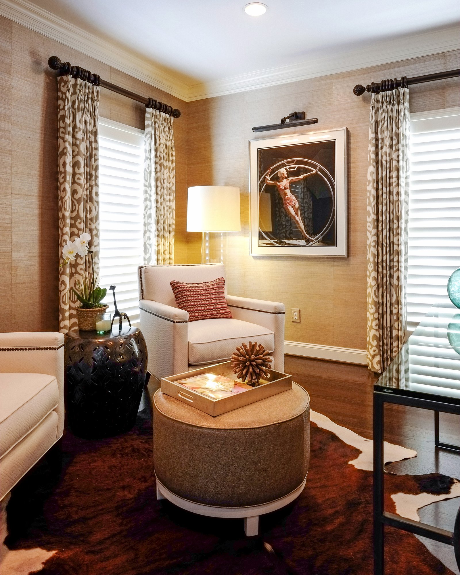 Bluff Run sitting room with grasscloth walls, a leather ottoman and framed art lit by a picture light
