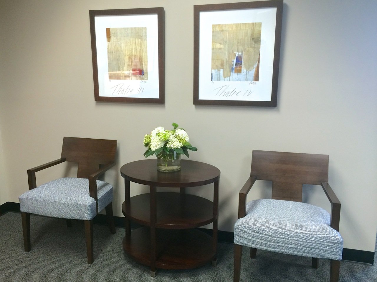 Pair of wood armchairs with blue upholstery around a round side table with white hydrangeas