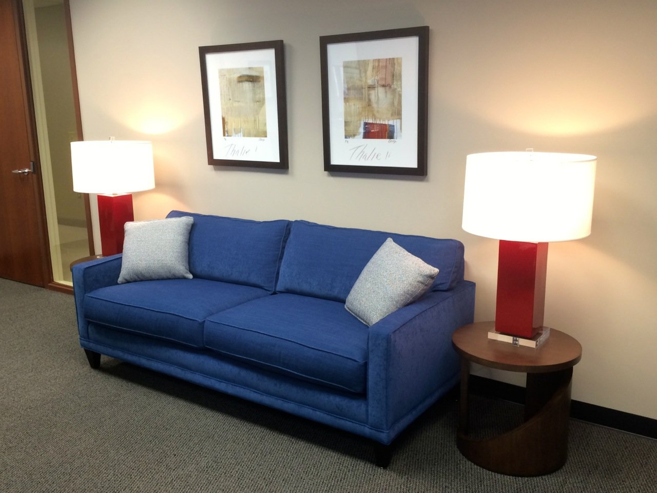 Blue sofa flanked by red lamps with a pair of framed abstract prints above