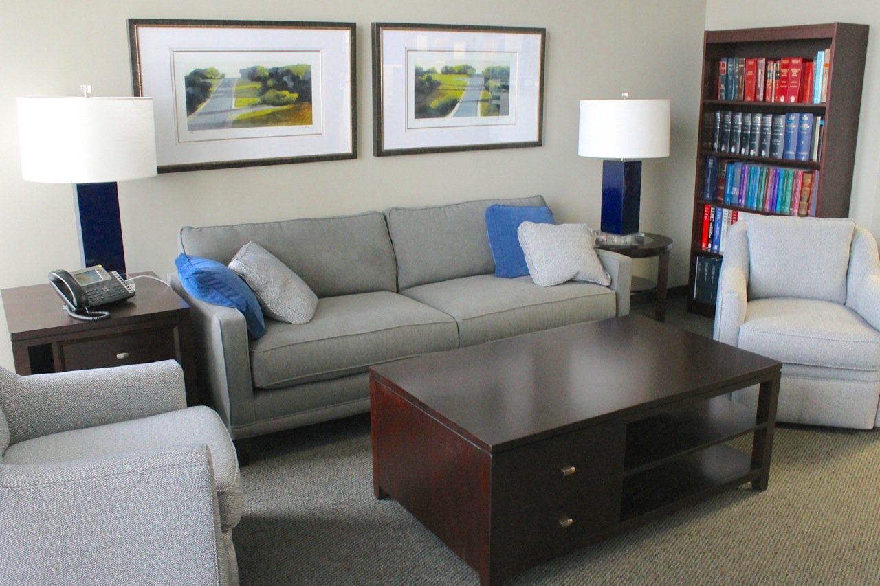 Relaxed seating area with a gray sofa, blue pillows, cobalt lamps, a dark coffee table and a wall of law books