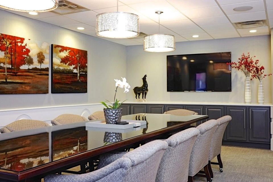 Conference table lined with gray upholstered chairs beneath drum pendants, with red tree paintings on the wall