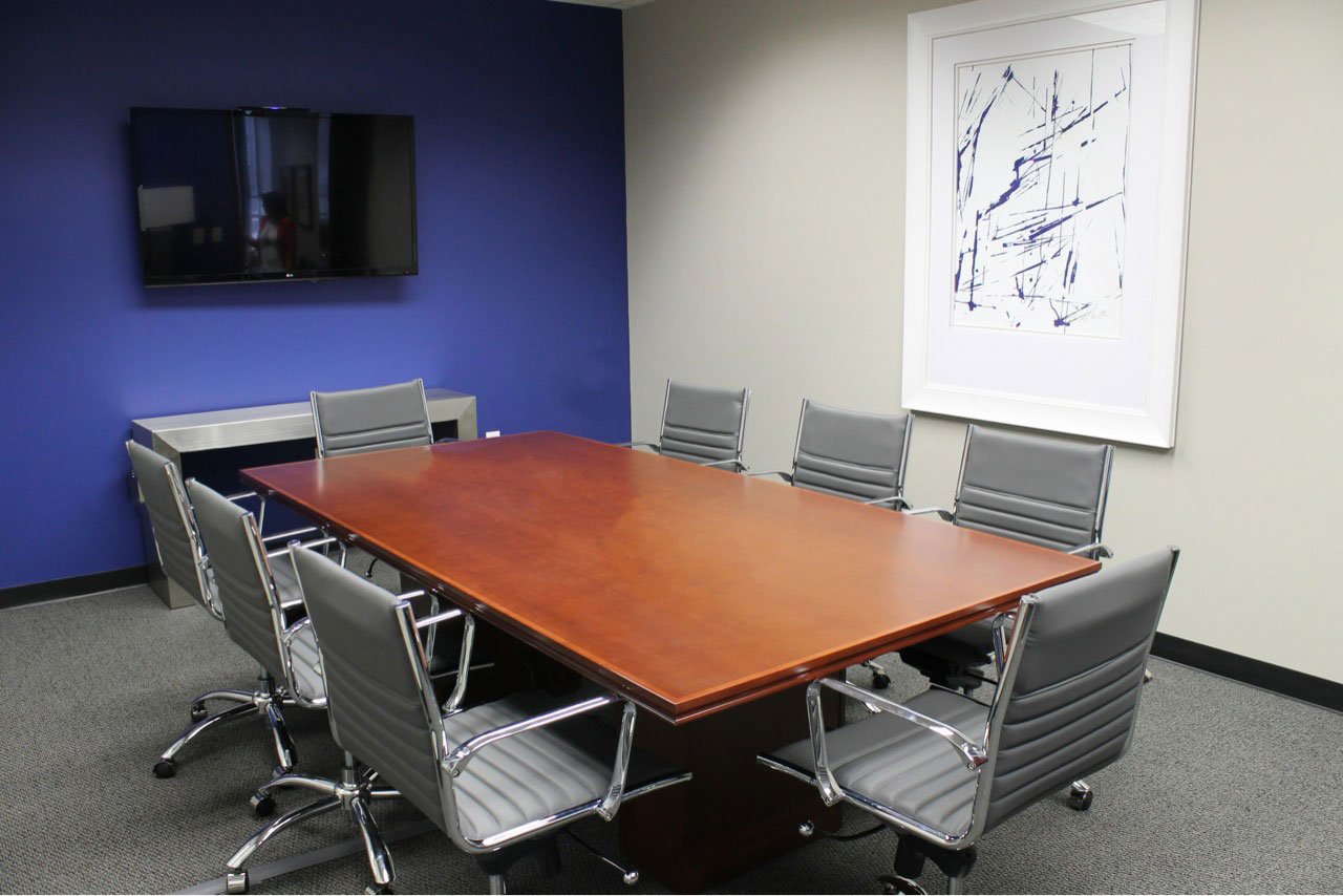 Meeting room with a blue accent wall, a cherry table, gray swivel chairs and a framed blue ink drawing