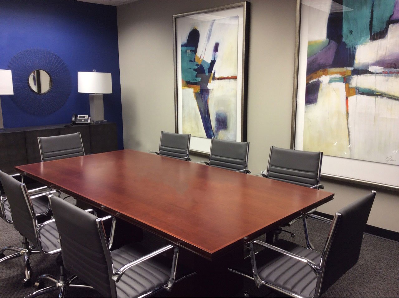 Conference room with a cherry table, gray leather chairs, a blue accent wall and large abstract paintings in blue and teal