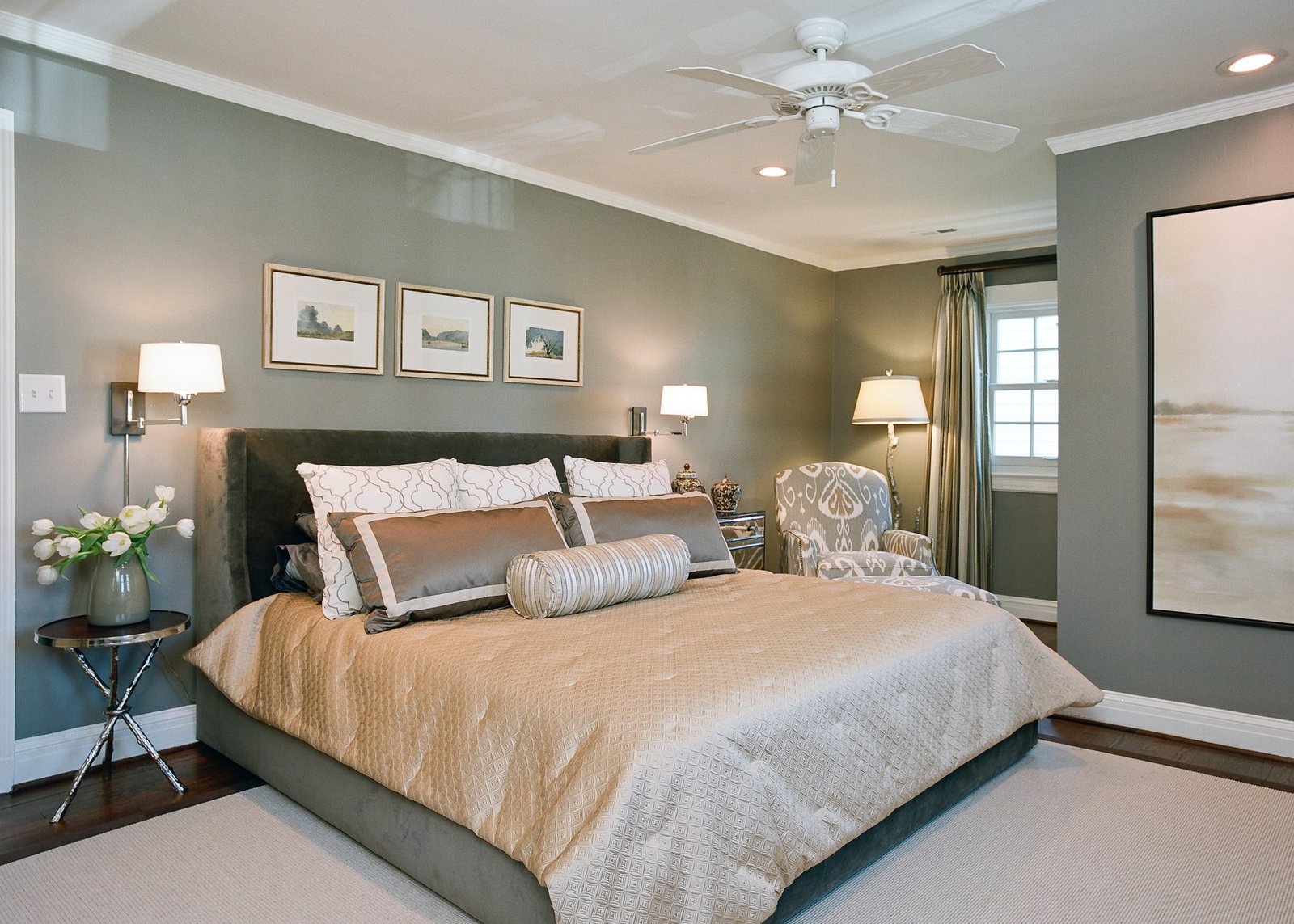 Serene sage bedroom with an upholstered bed, satin bedding, a trio of framed landscapes and a patterned armchair