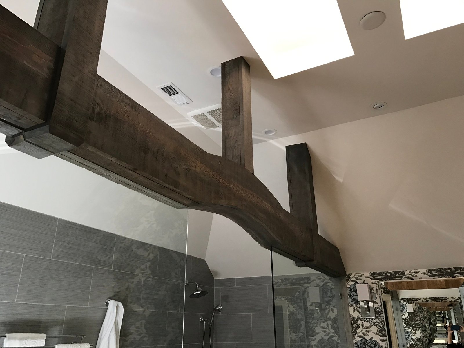 Rustic timber beams beneath a skylight in the vaulted bath ceiling
