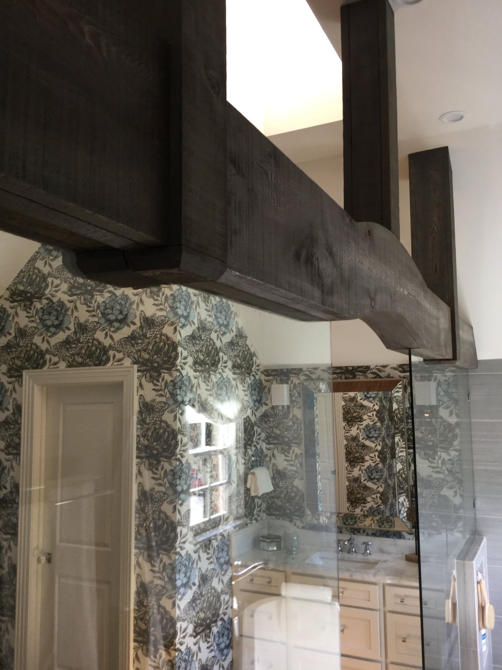 Timber beam and botanical wallcovering above the glass shower enclosure