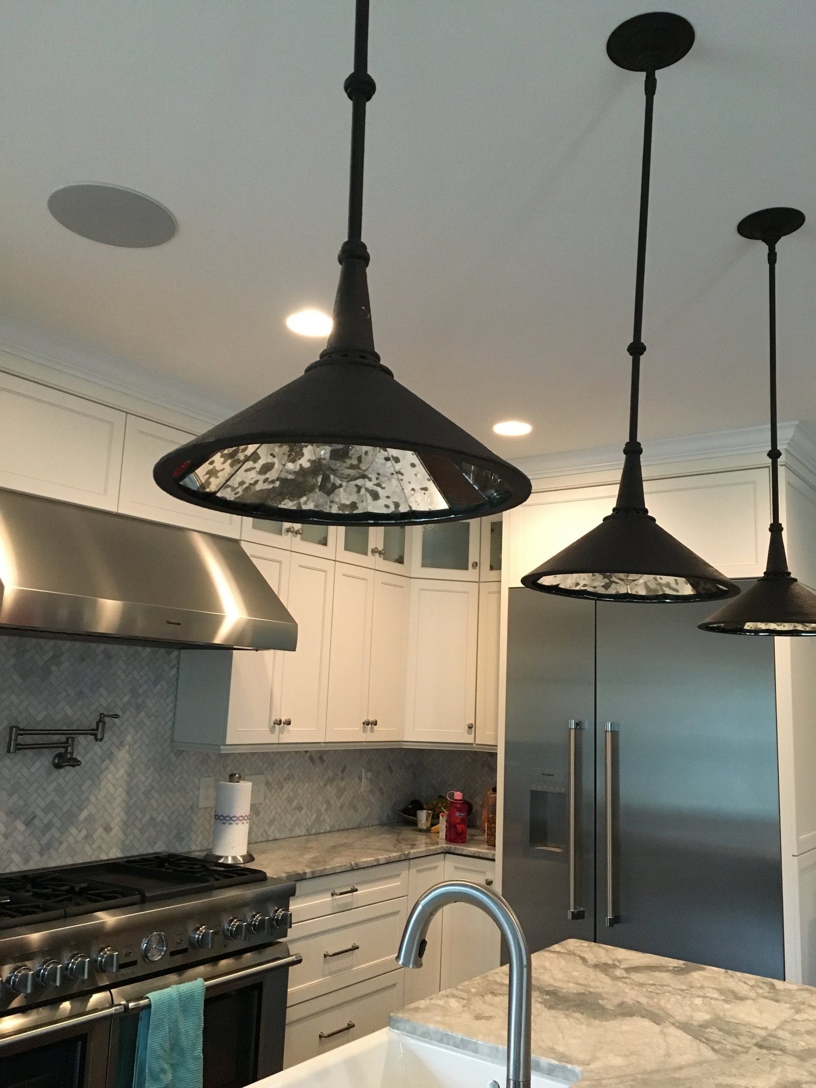 White kitchen with black cone pendants over a marble island and a professional range