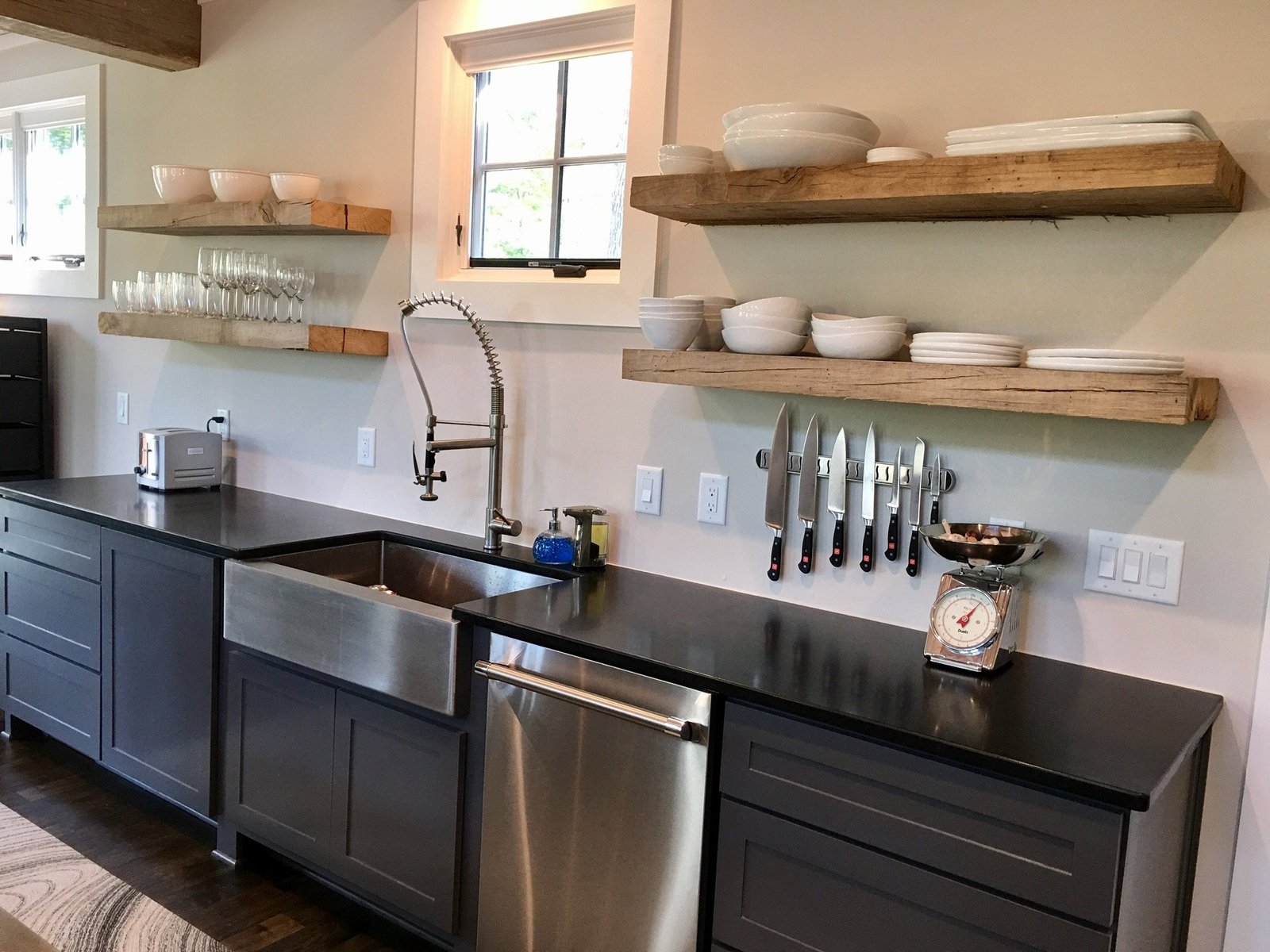 Floating reclaimed-wood shelves over a stainless farmhouse sink, black counters and slate cabinetry