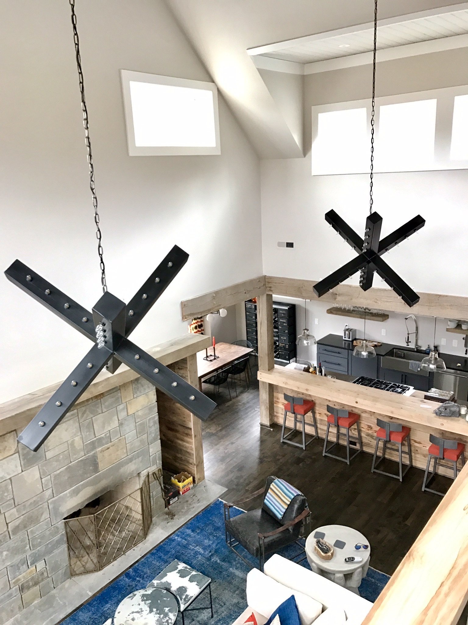 View from above into a great room with black X-shaped light fixtures, a stone fireplace and the kitchen beyond