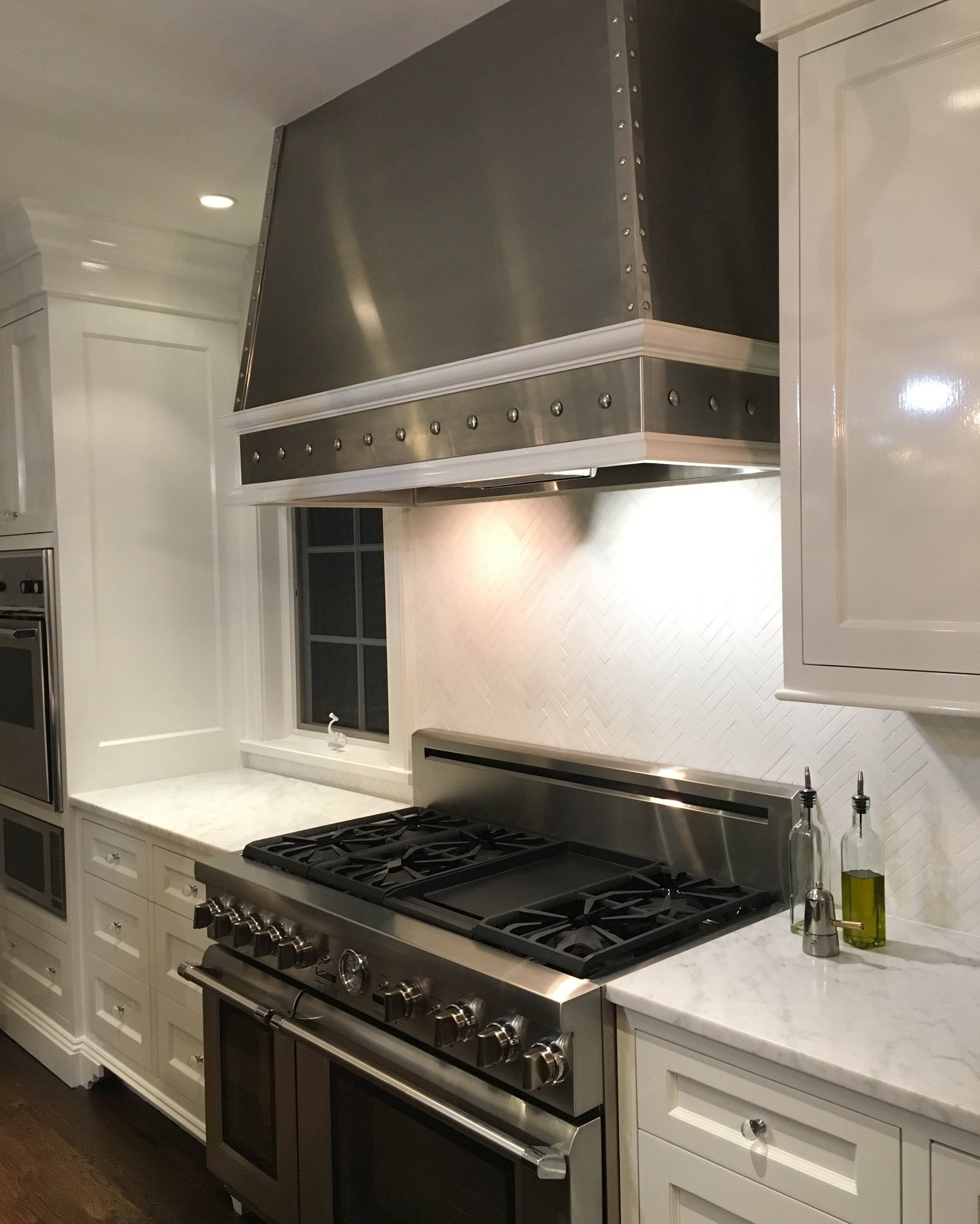 White kitchen with a studded metal range hood, marble backsplash and professional range