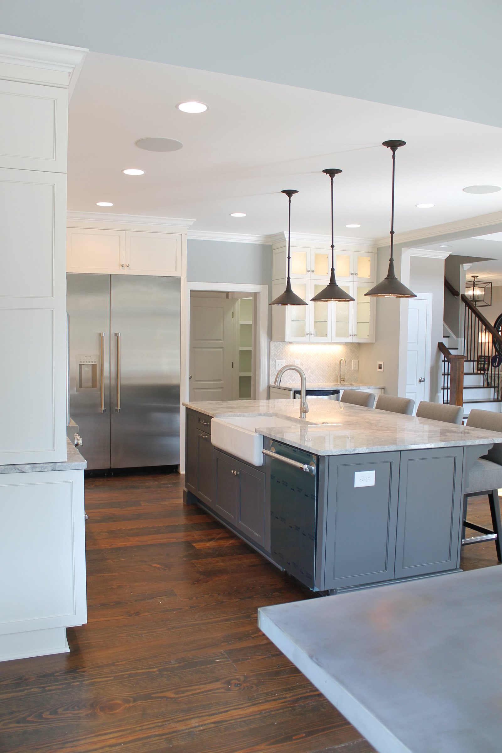 White kitchen with a slate-blue island, farmhouse sink and trio of pendant lights