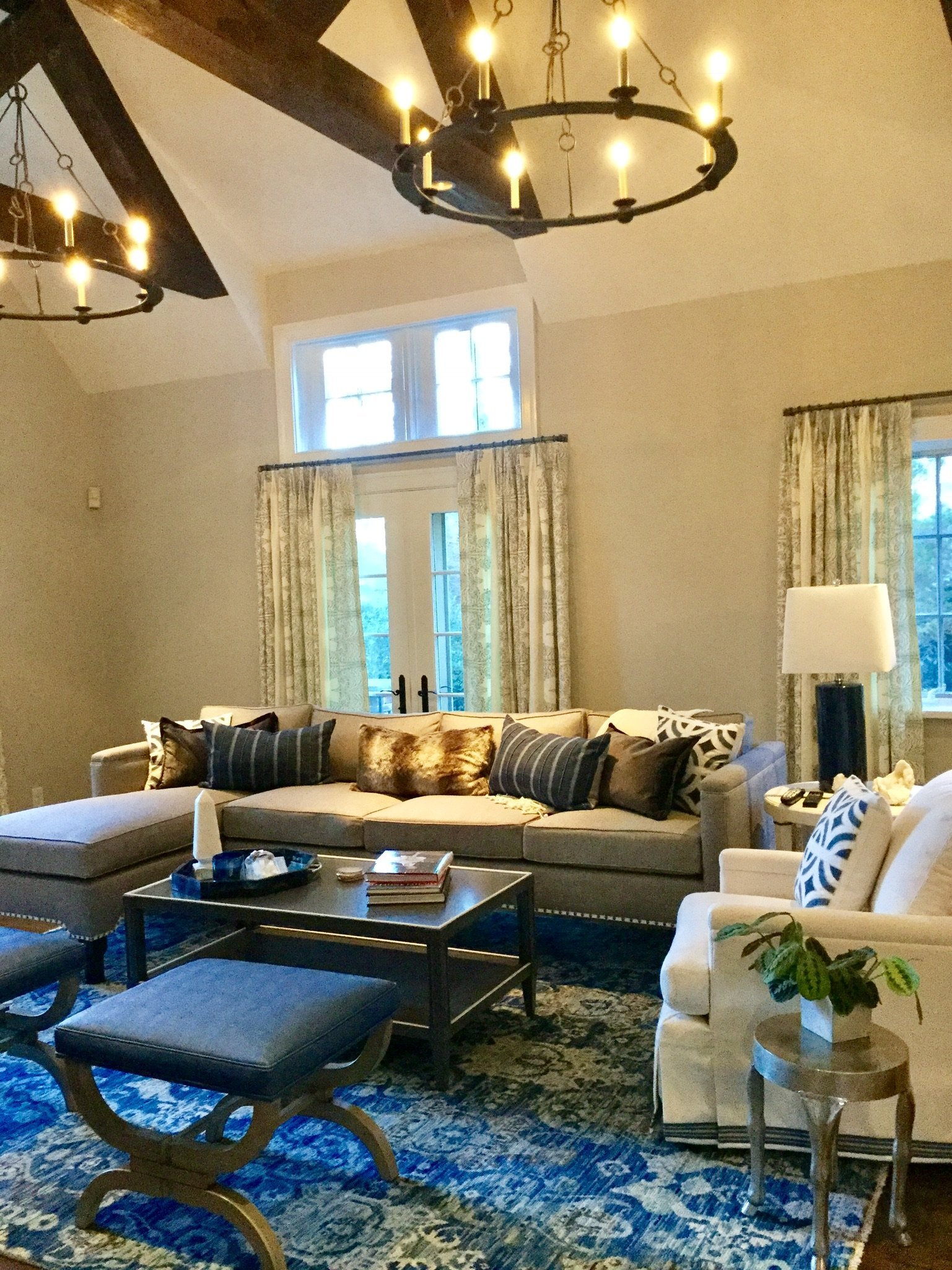 Vaulted living room with a ring chandelier, blue x-base benches on a patterned rug and a deep sectional