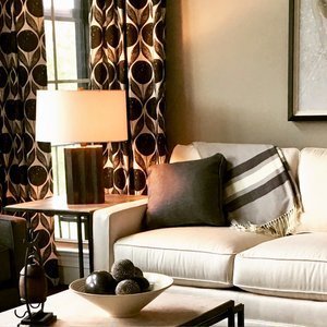 Cream sofa with a striped throw beside a lamp and bold patterned drapery