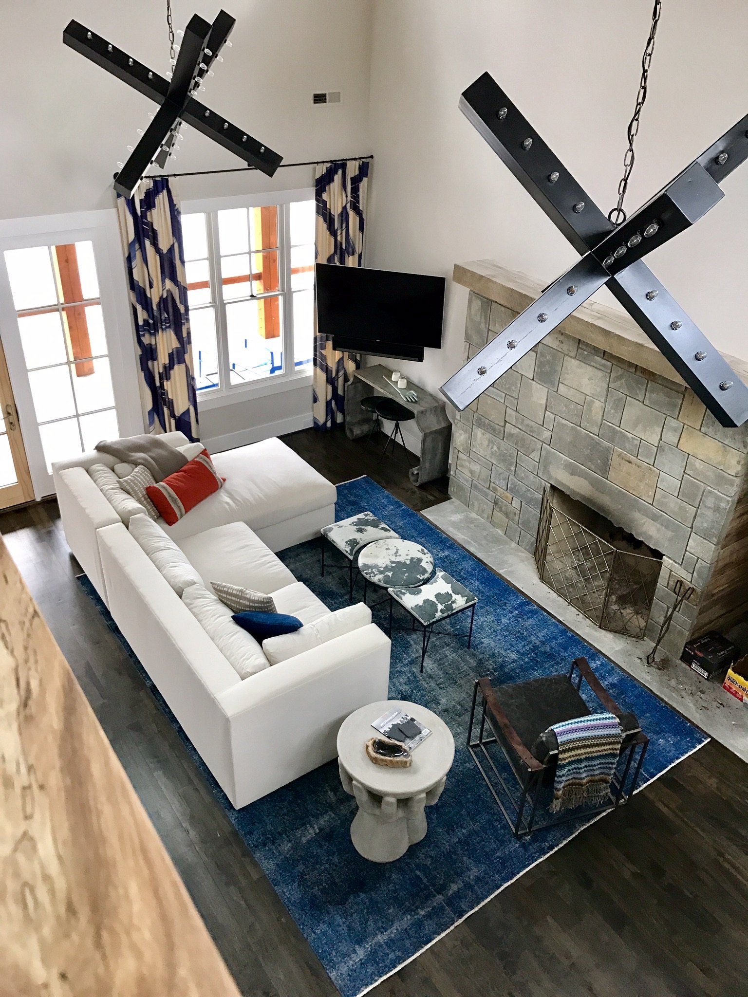 Two-story great room seen from above, with black X-shaped light fixtures, a white sectional, a stone fireplace and an indigo rug