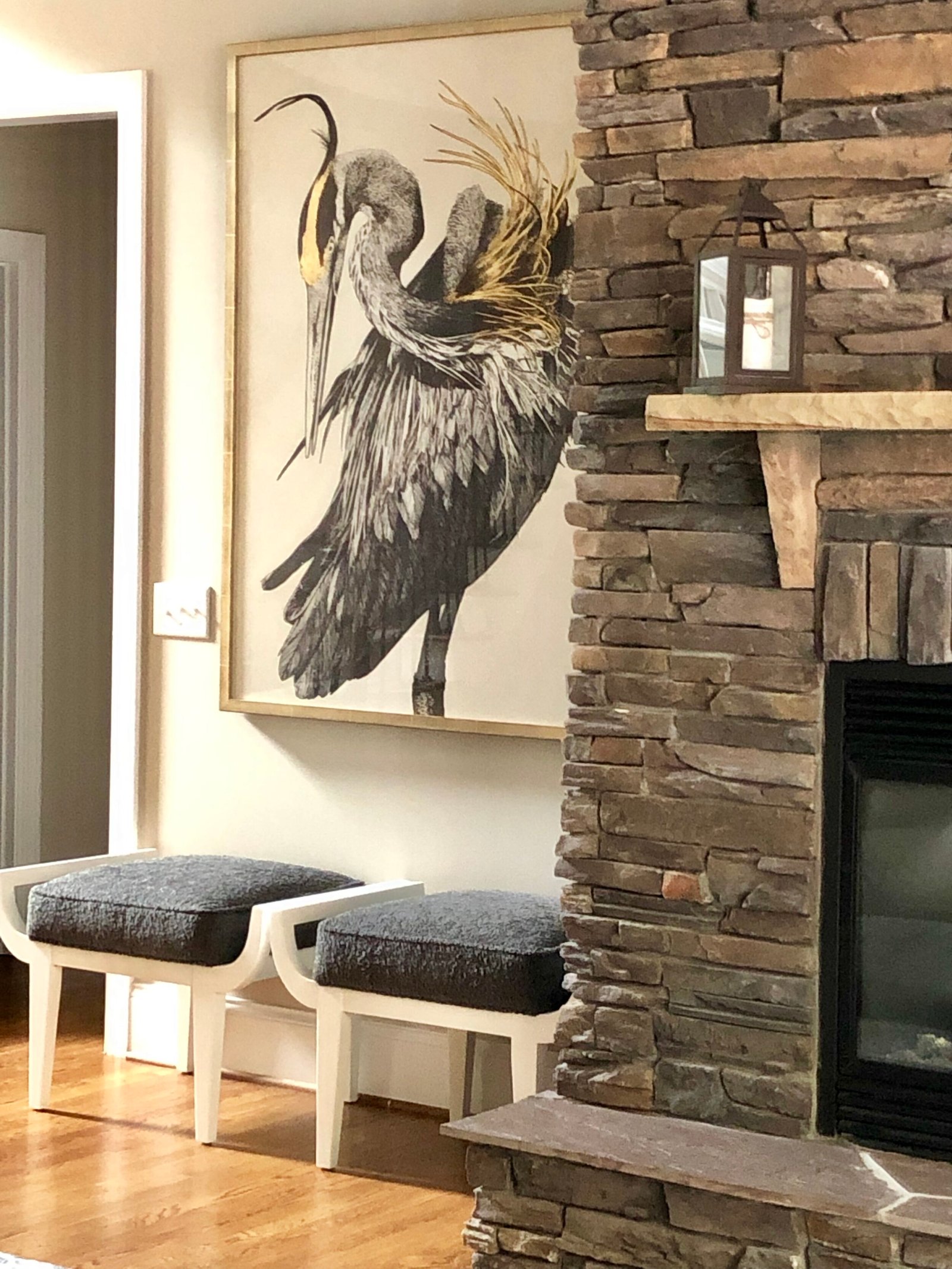Stacked-stone fireplace beside a large heron artwork and a pair of upholstered benches