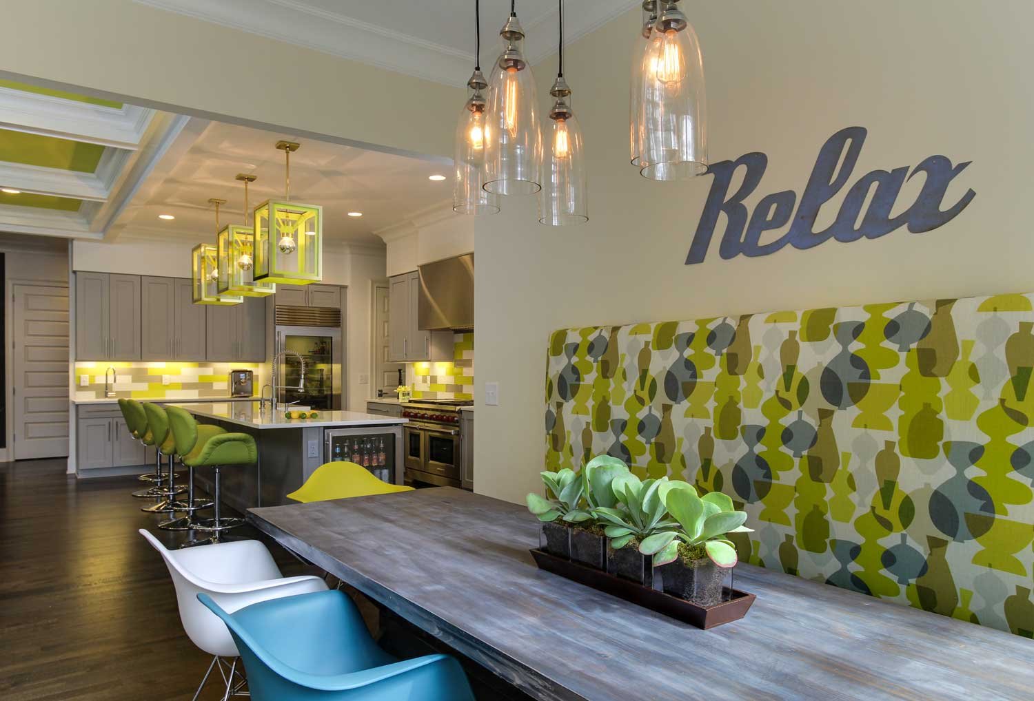 Kitchen and dining area with chartreuse lantern pendants, a patterned banquette and a Relax wall sign