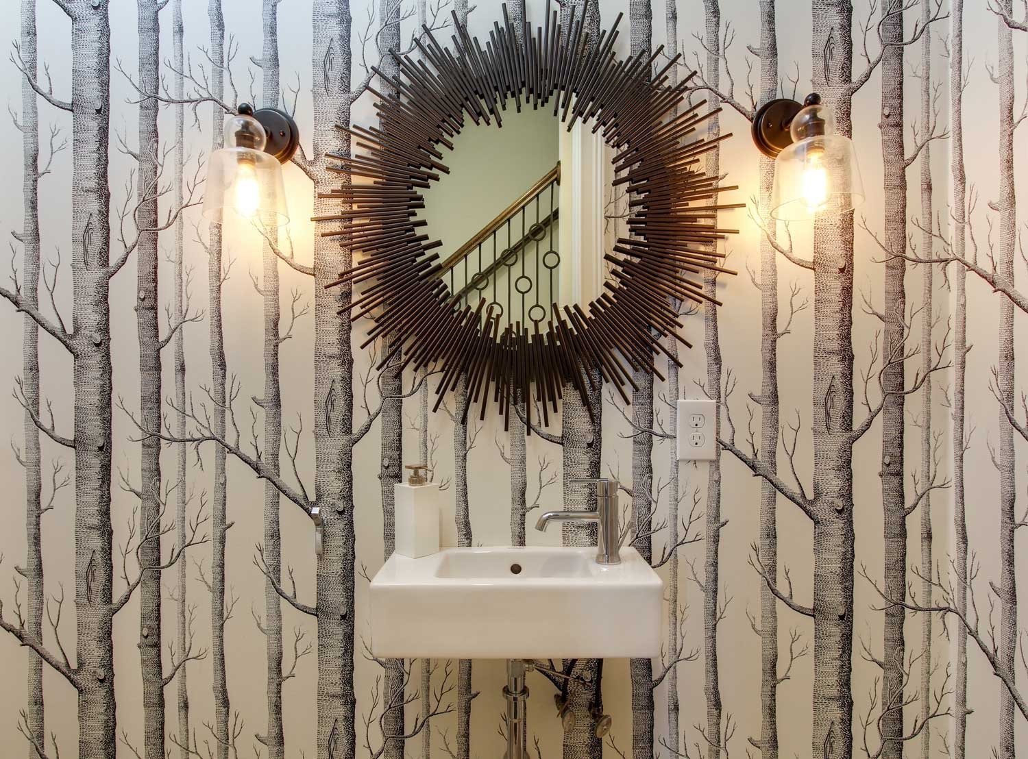 Powder room with birch-tree wallpaper, a spiked sunburst mirror, glass sconces and a floating white sink