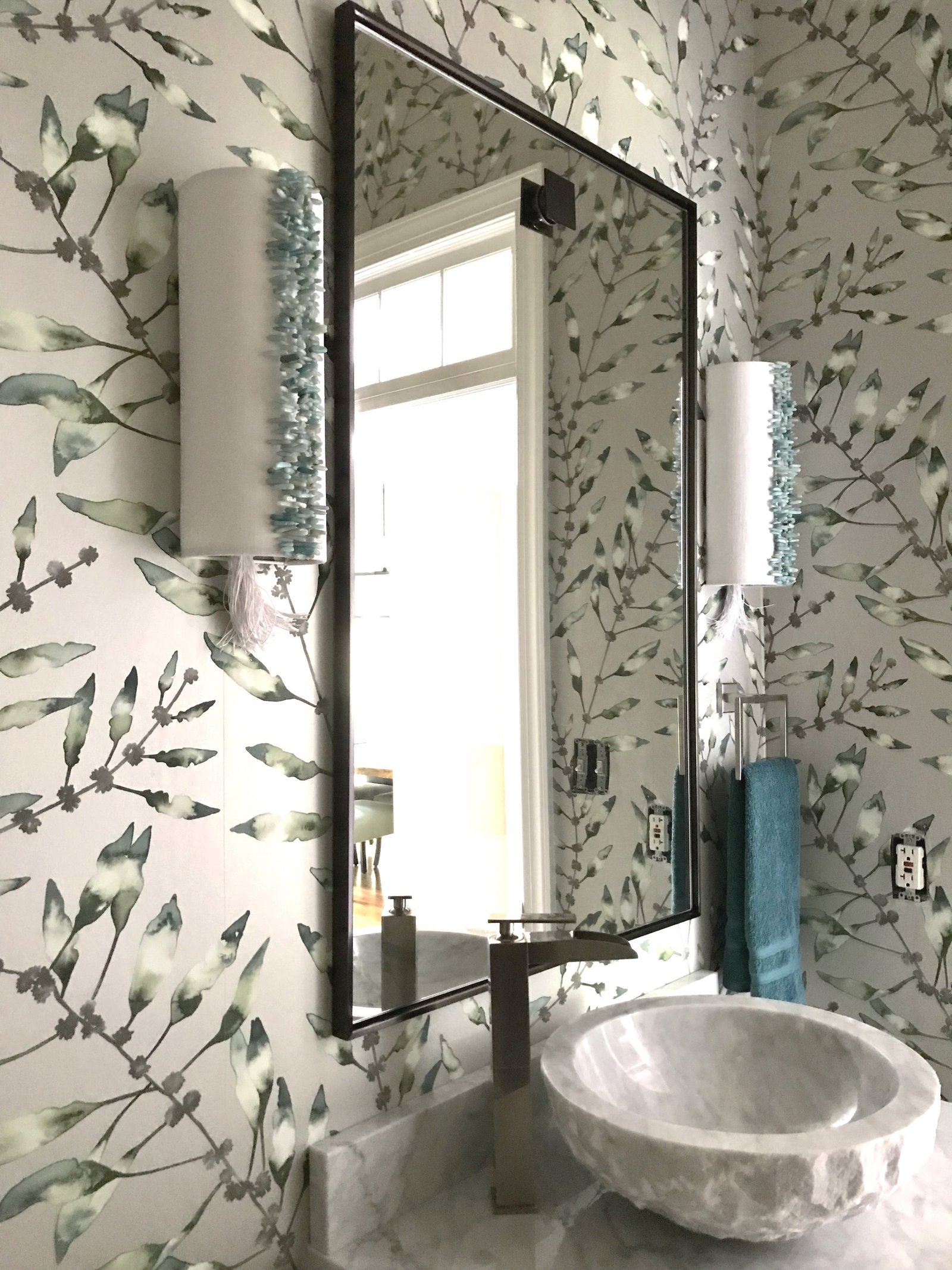 Powder room with botanical wallpaper, a carved stone vessel sink and a slim black mirror