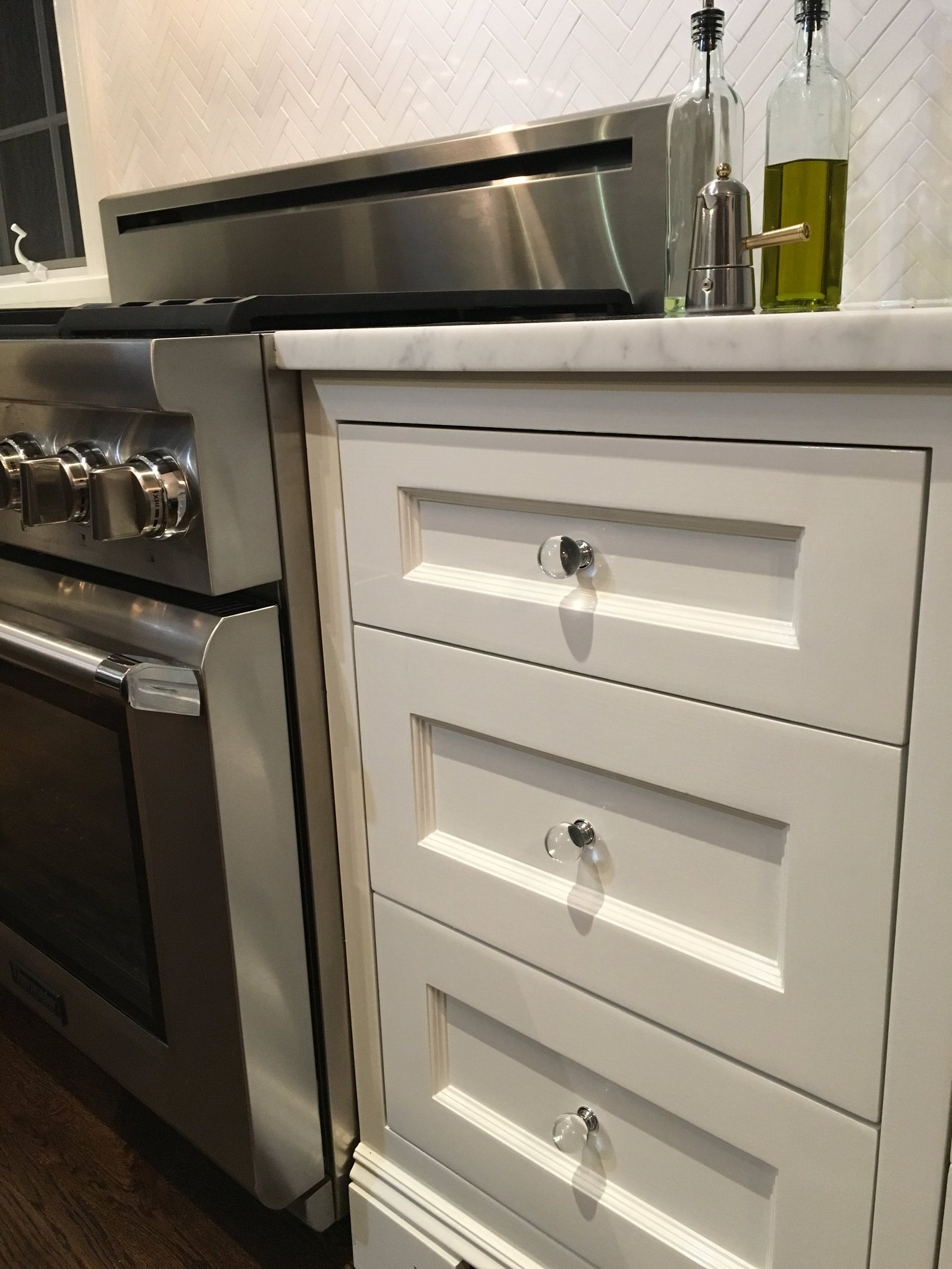 White shaker drawers with crystal knobs beside the professional range