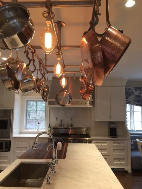 Copper pots hanging from a pot rack above a marble-topped island
