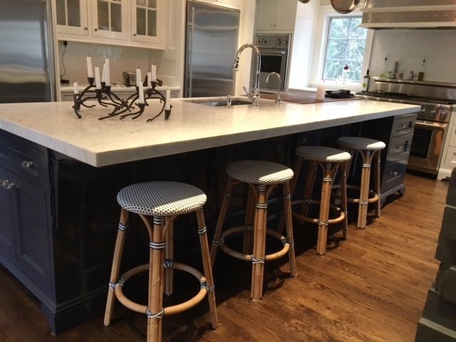 Kitchen island with a white marble top, dark base and rattan counter stools