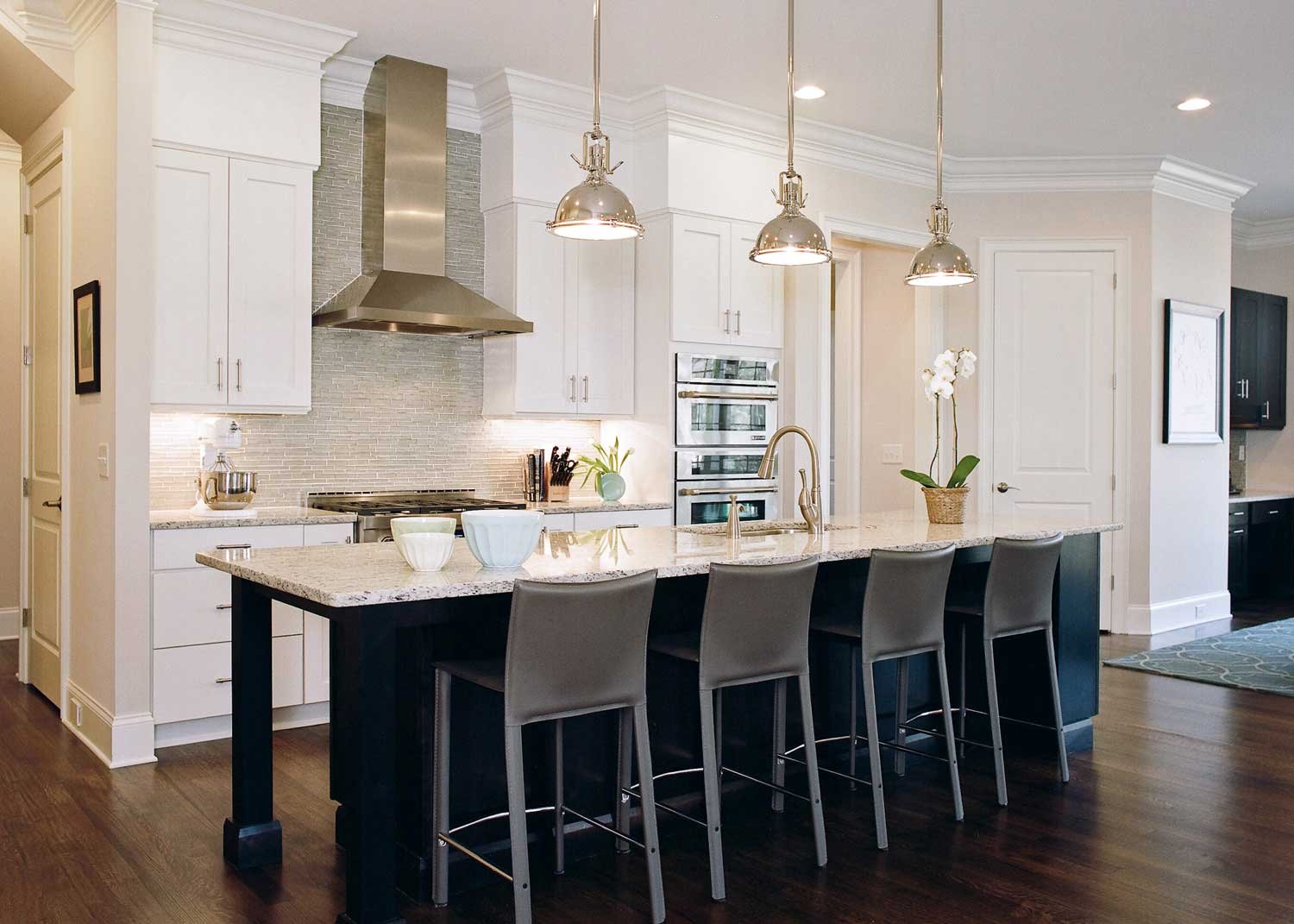 White kitchen with a black island, bell pendants and a stainless hood