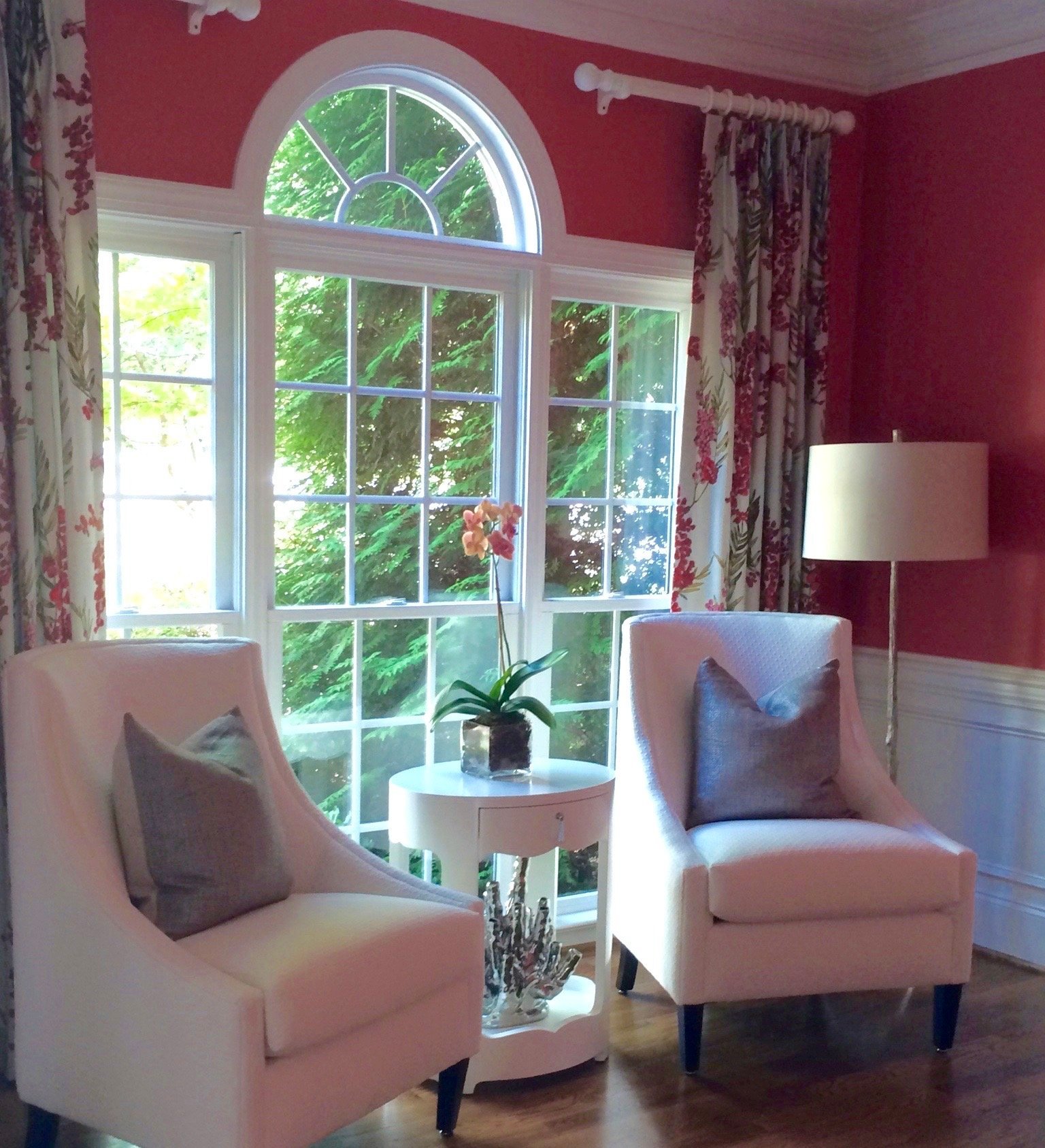 Sitting room with raspberry walls, an arched window and a pair of blush upholstered chairs