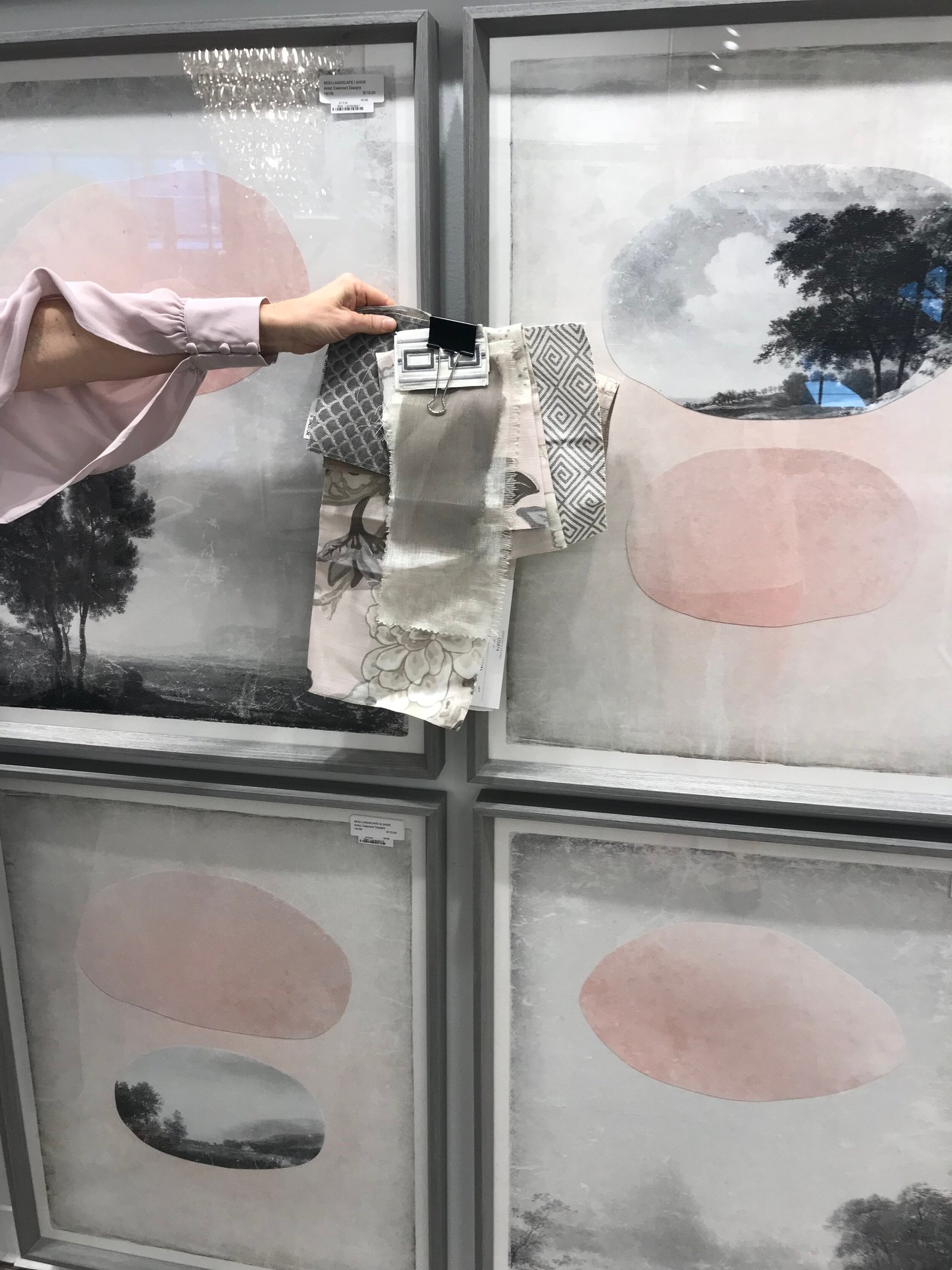 A designer holds fabric swatches against framed artwork while sourcing in a furniture showroom