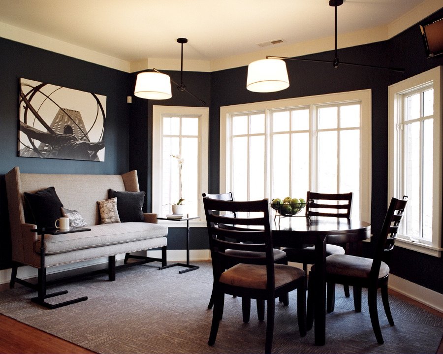 Breakfast room with deep navy walls, drum pendants, an upholstered settee and a round table beneath tall windows